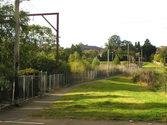 Looking north along the old mainline formation north of the station. The overhead remains, as do two sets of tracks, though the latter are buried beneath significant overgrowth.