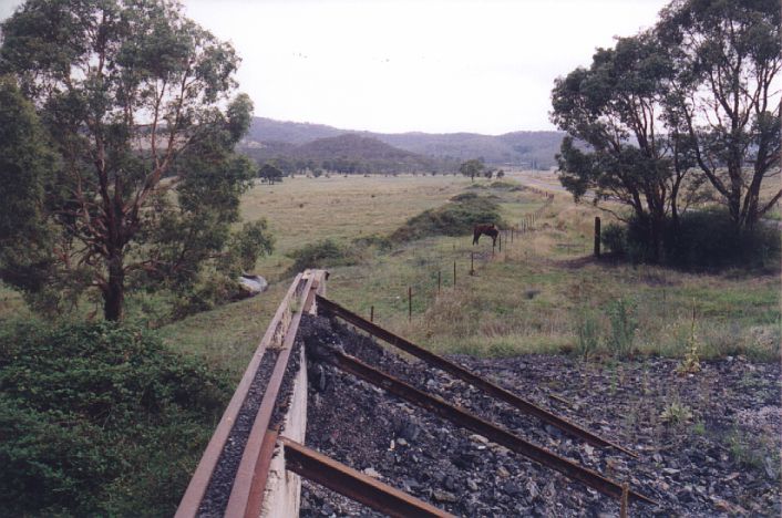 
Cullen Bullen was the junction for a short branch to the Invincible Colliery.
Near the junction is the remains of a coal bunker.  The formation is
visible behind the wall, and continues along the road in the distance
for a couple of kilometres.
