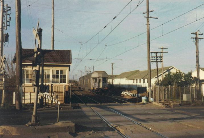 
Parramatta Road Signal Box controls the level crossing with the busy main
road.  The line often featured shortened trains due to lack of
available power on the line.  The two car set is about to cross
the road and terminate at Clyde station. Note also the spare booms arms -
the booms at this crossing have a short lifespan due to inattentive
car drivers!
